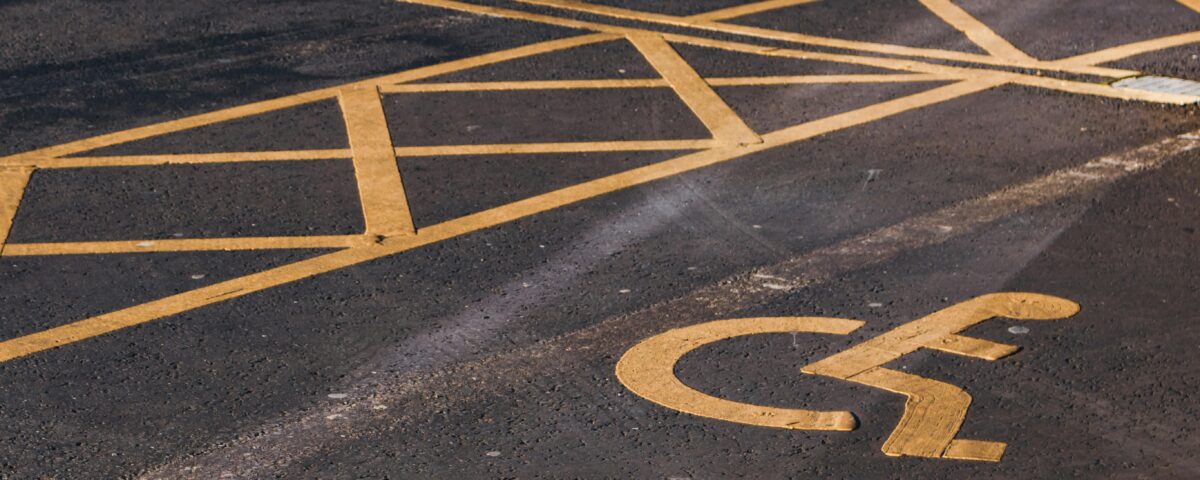 An accessible parking bay with the international symbol of access (person in a wheelchair) painted on the tarmac in yellow.