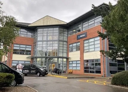 Picture1 An image of a graphic showing the exterior of a SpaMedica building on an overcast day. Out front is a car park with a black taxi van parked outside the entrance. To the right is an empty accessible parking bay.