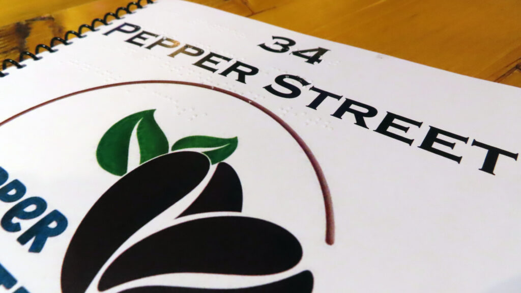 A close up photograph of the 34 Pepper Street cafe menu, highlighting the braille elements embedded the front cover.