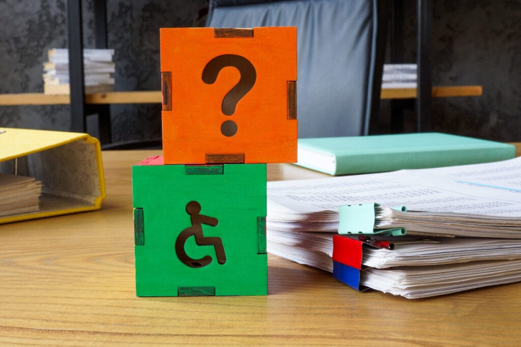 An office desk has two cardboard cubes (the top is red, the bottom is green) stacked on top of each other. These are to represent the question of what makes something accessible. The red one has an image of a question mark on it, while the green one features the international symbol of access.