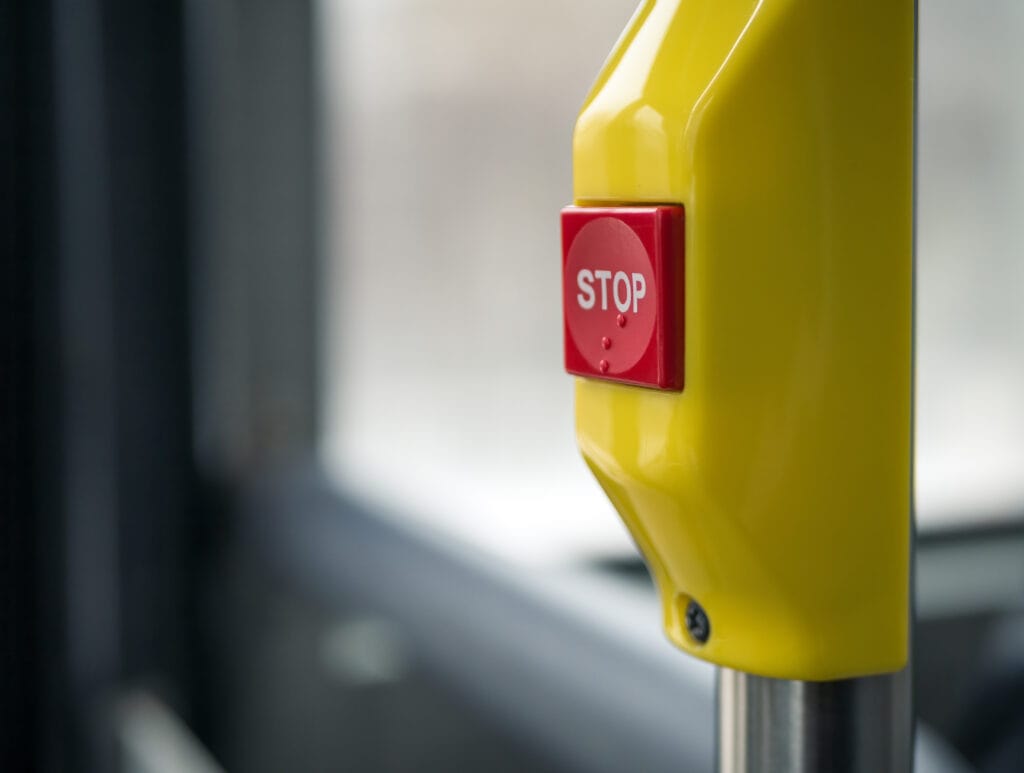 A close up narrow focus photograph of a red bus stop button with raised braille printed to the face.