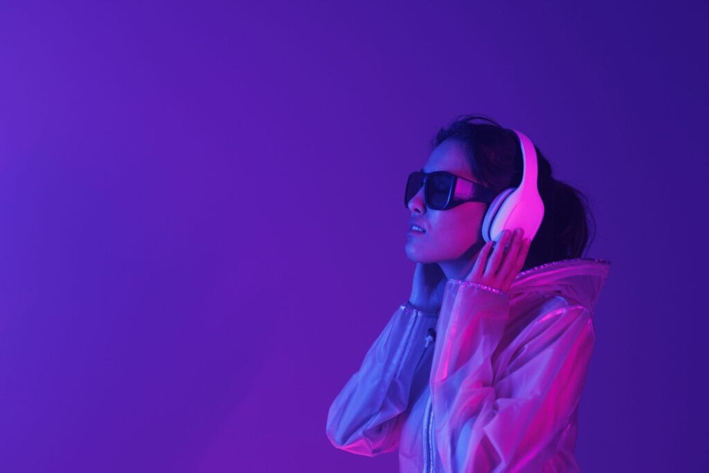 A pretty young woman wearing dark glasses and headphones in a sensory room, which is lit up purple.