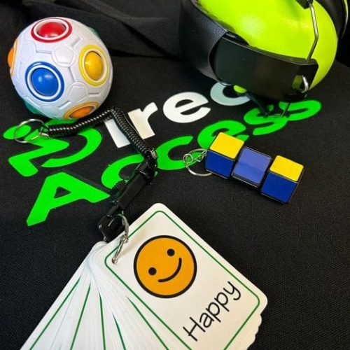 369989518_698408568950435_3258434858085169734_n A range of green sensory items including communication cards, headphones and a multi-coloured fidget toy placed on top of a black t-shirt with text that reads Direct Access in white and green.