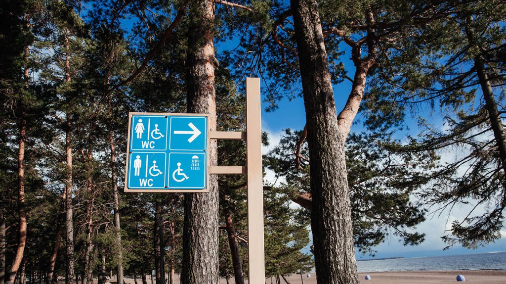 WC and shower sign in the forest. WC for disabled. Beach resort. Sea and beach in the background.