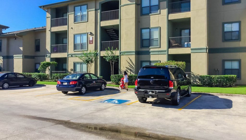 Typical apartment complex building in suburban area at Humble, Texas, US. Parked cars on uncovered parking lot along apartment blocks with reserved parking sign for van disable or wheelchair drivers.