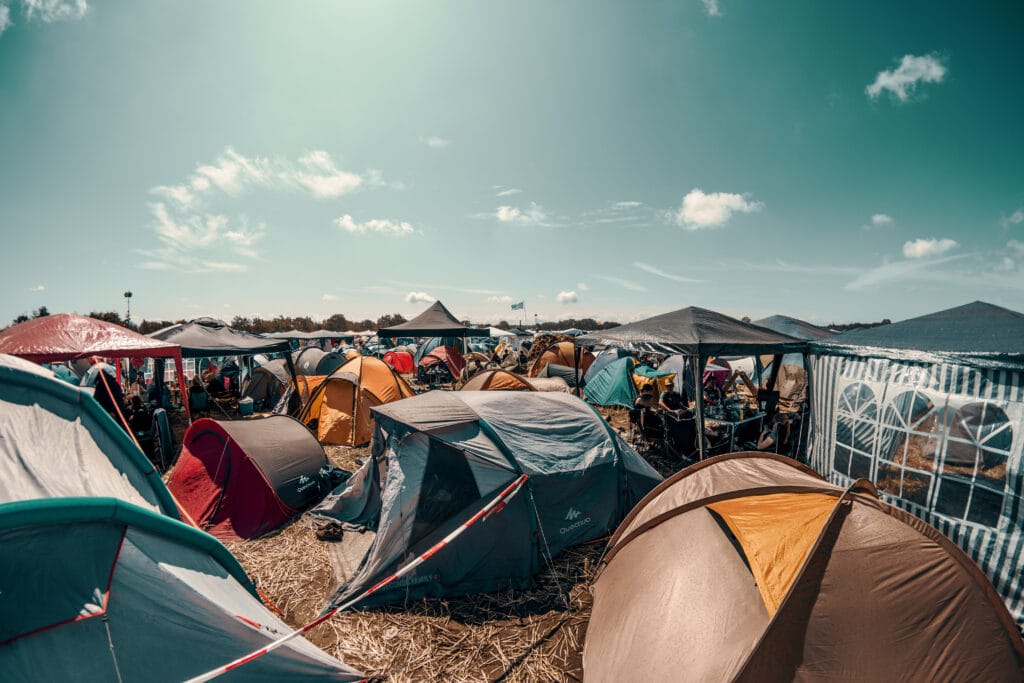 A campsite at a festival during a summers day Multiple tents are all set up and crowded compactly together in a field laid down with straw.
