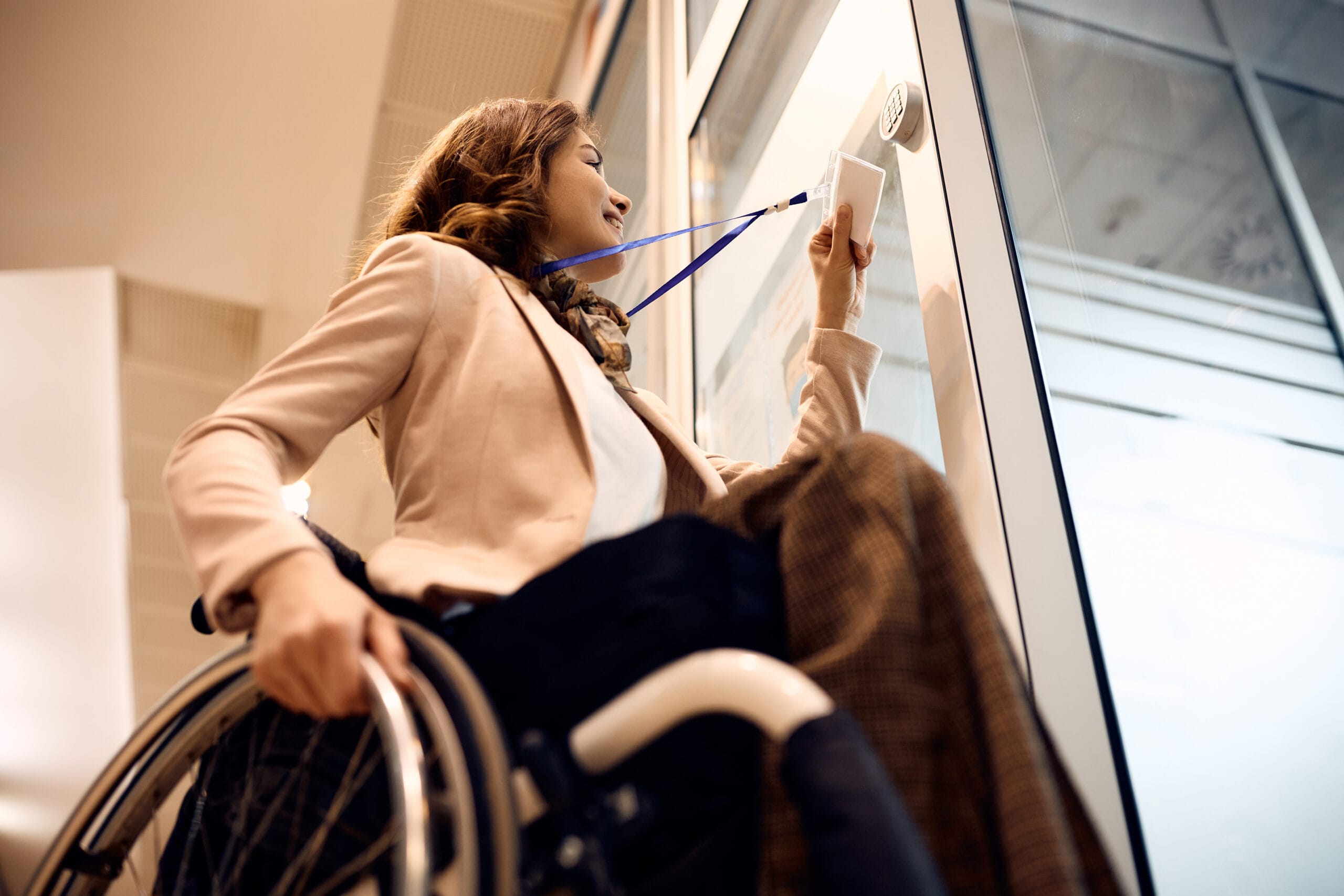 Happy wheelchair-bound businesswoman opens an office door with her ID card.