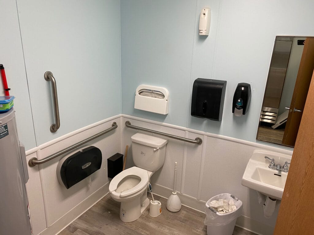 An example of an accessible restroom featuring grab rails, sufficient space for a wheelchair user, a low wall mirror and single lever taps.