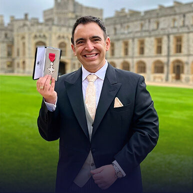 Steven Mifsud holding his MBE on the grounds of Windsor Castle while smiling for a photo.