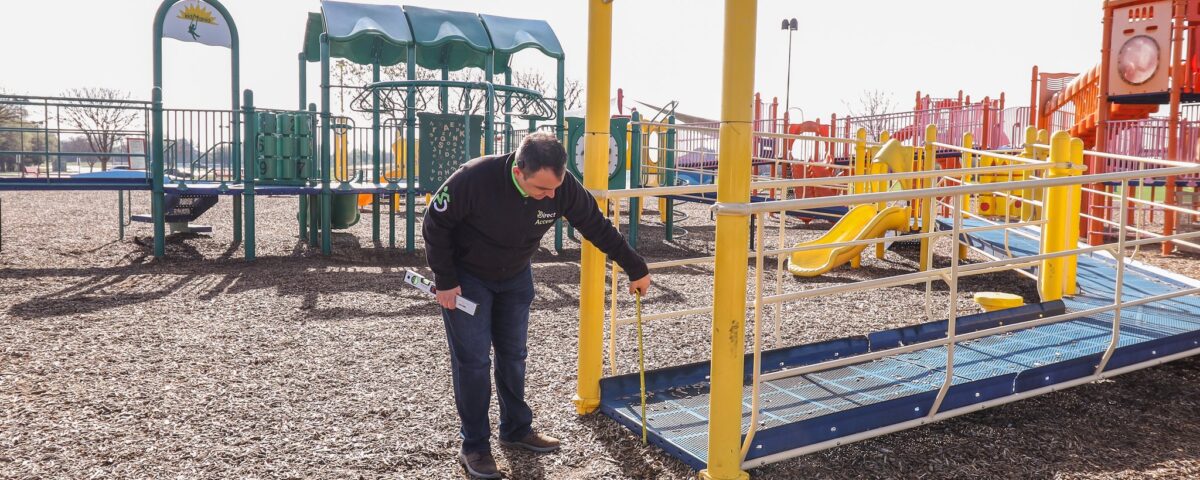 A middle aged man inspects the height of a drop from a ramp at a children's playground.