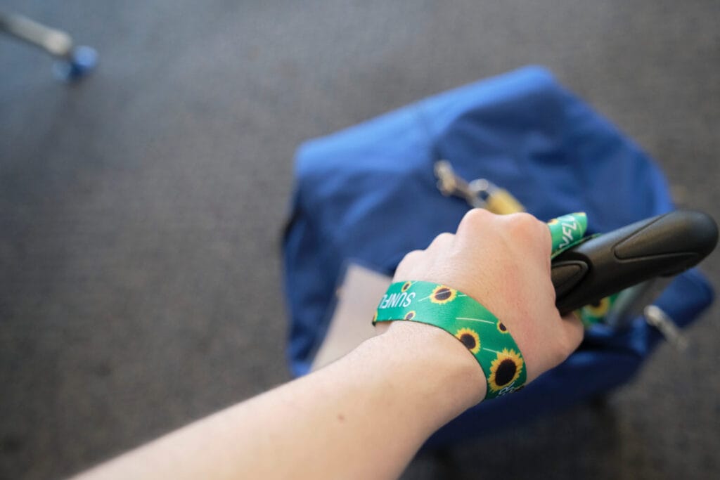 Hand of an unrecognizable person dragging a suitcase, wearing on the wrist a lanyard of sunflowers, symbol of people with invisible or hidden disabilities.