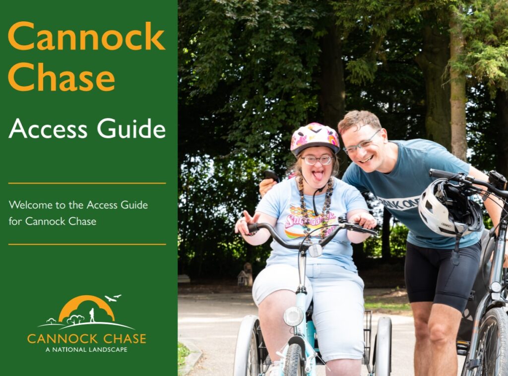 A photograph of the front cover of the Access Guide which Direct Access produced for Cannock Chase. The cover has a dark green colour scheme with a mixture of yellow and white text. It reads "Cannock Chase access guide. Welcome to the Access Guide for Cannock Chase". Underneath this text is the Cannock Chase logo. A photograph on the cover shows a young white woman with downs syndrome riding a bike with stabilisers joyfully. Next to her getting in close for a photo is a white male companion who is off his bike and holding it with one hand. He is also smiling happily. Behind them is a bike trail through some woods.