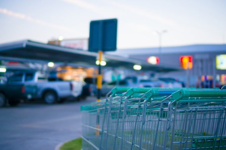 A row of shopping carts at the entrance of a supermarket next to a parking lot.