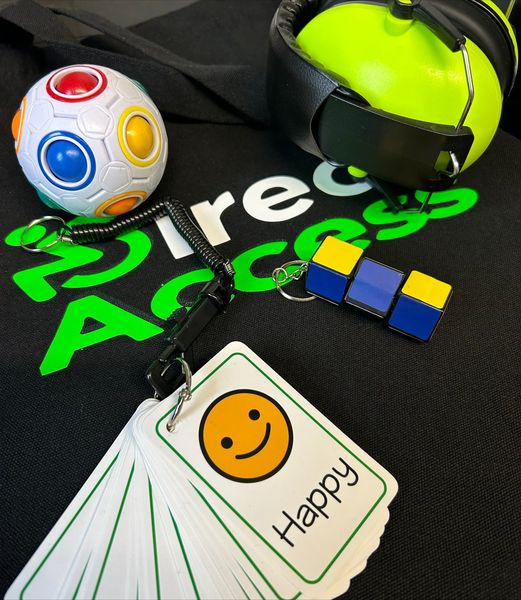 A range of green sensory items including communication cards, headphones and a multi-coloured fidget toy placed on top of a black t-shirt with text that reads Direct Access in white and green.