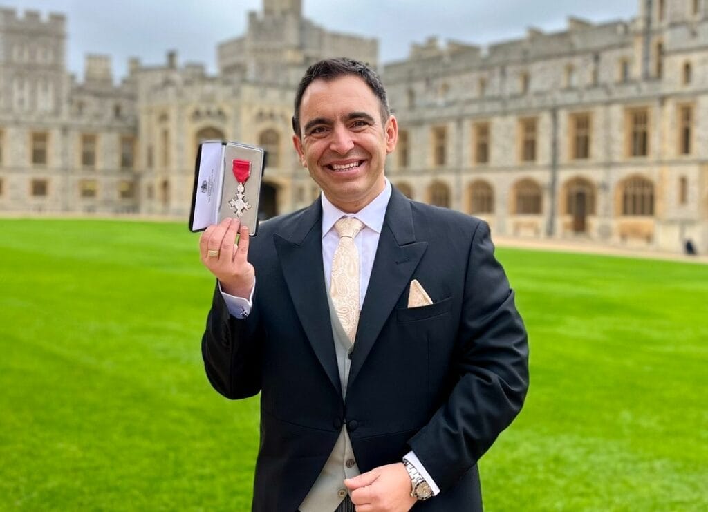 Steven Mifsud holding his MBE medal on the grounds of Windsor Castle on an overcast morning.