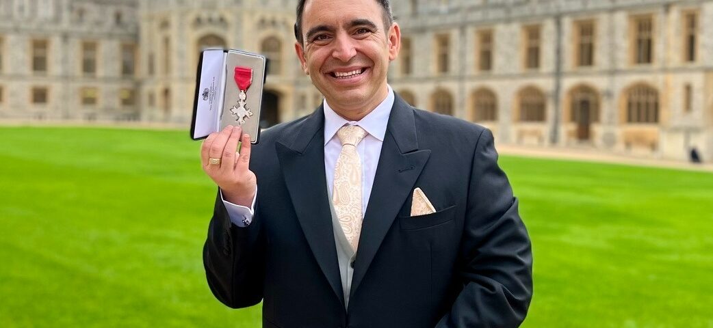 Steven Mifsud holding his MBE medal on the grounds of Windsor Castle on an overcast morning.