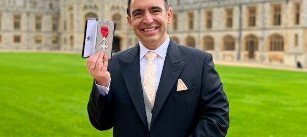 Steven Mifsud holding his MBE medal on the grounds of Windsor Castle on an overcast morning.