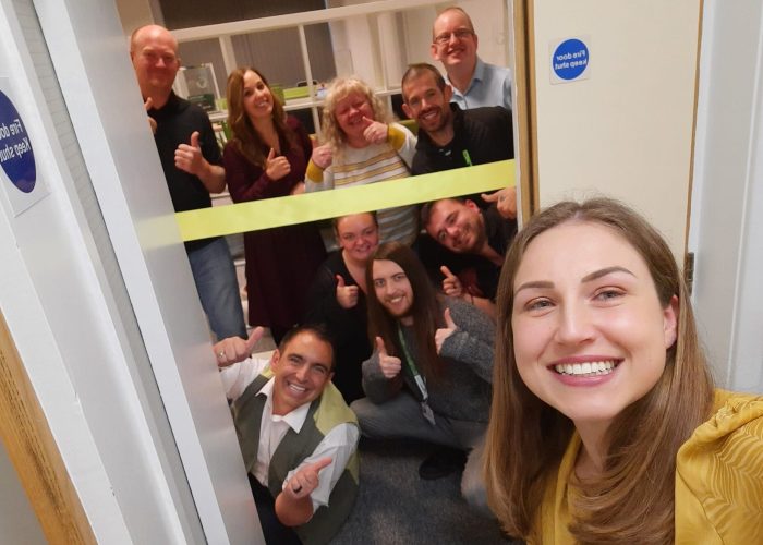 316946696_535949428529684_5988721729878979786_n-e1669825439139.jpg A group photo of the full Direct Access Team at the grand opening of the office. A yellow banner ready to be cut is stretched across the door.