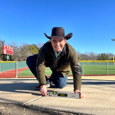 Direct Access founder Steven Mifsud MBE measuring the level of a concrete pathway with a baseball field in the background.